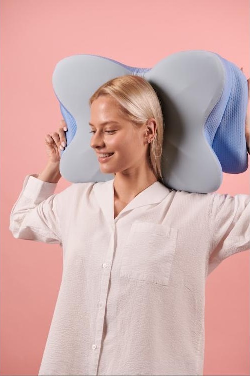 Woman holding the ergonomic butterfly-contour pillow against her neck and shoulders